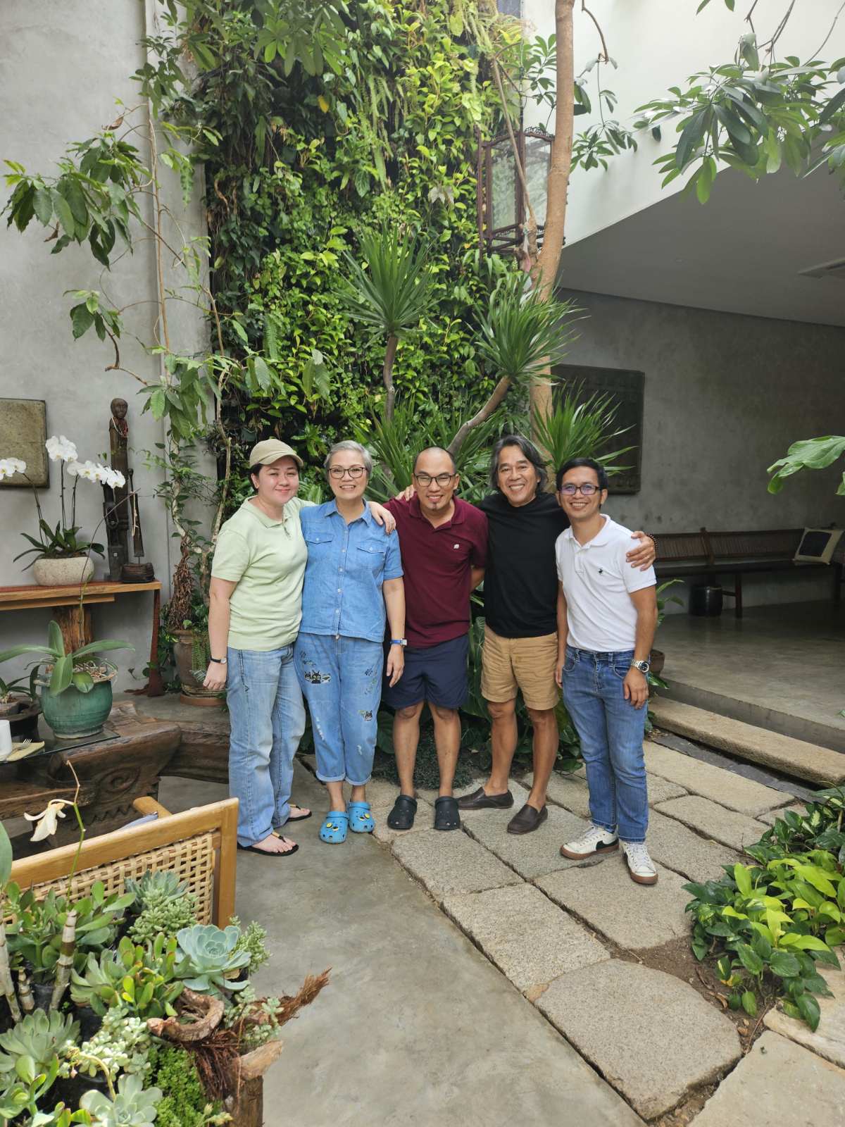Dr. Joel Orosa Paraiso (in black shirt) welcomes guests to his home. Behind them is the curtain of greens watered by a mechanical system. The elevated floor on the right situates his comfortable bed, facing the sala.